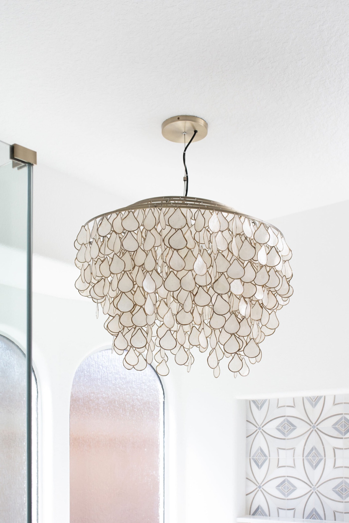 Capiz shell petal chandelier hung above the tub against a white ceiling in the Sunstream Bath project by Jennifer Kizzee Design