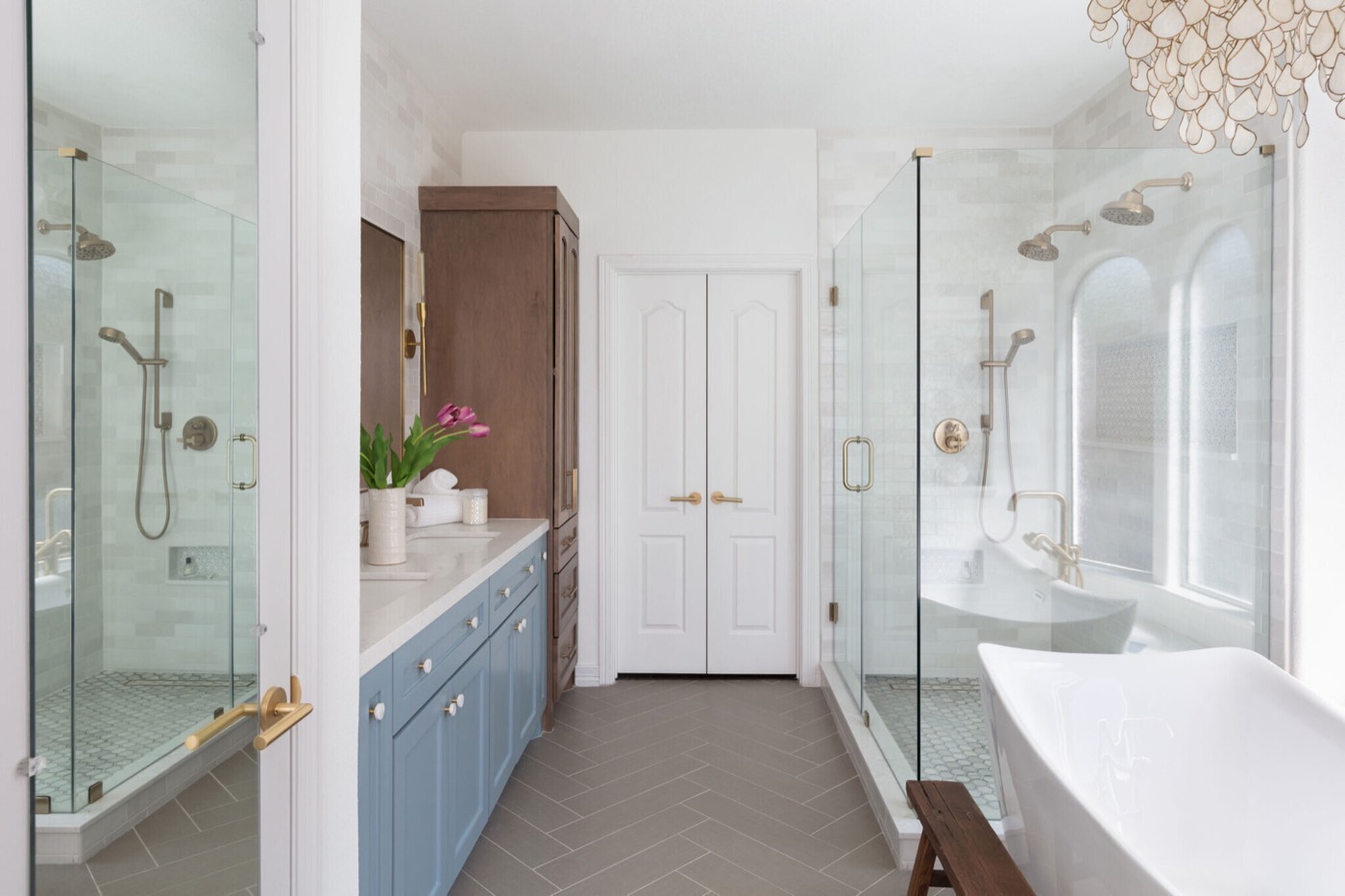 Two glass shower enclosures flanking the dusty blue vanity above a greige herringbone tile floor in the Sunstream Bath project by Jennifer Kizzee Design