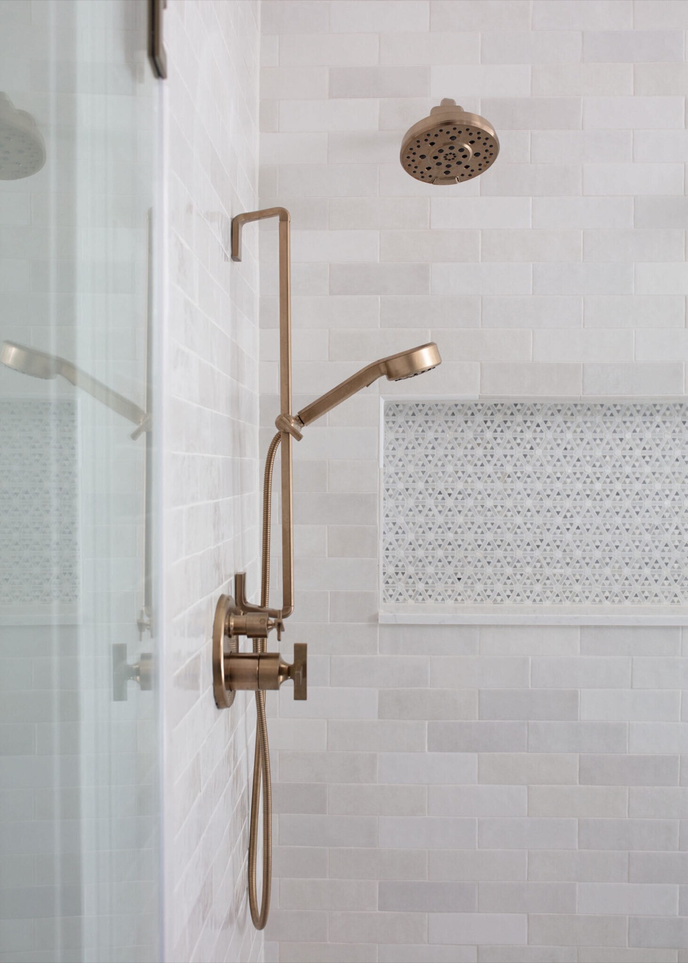 Champagne bronze handshower and rain head beside a penny round mosaic niche in the Sunstream Bath project by Jennifer Kizzee Design