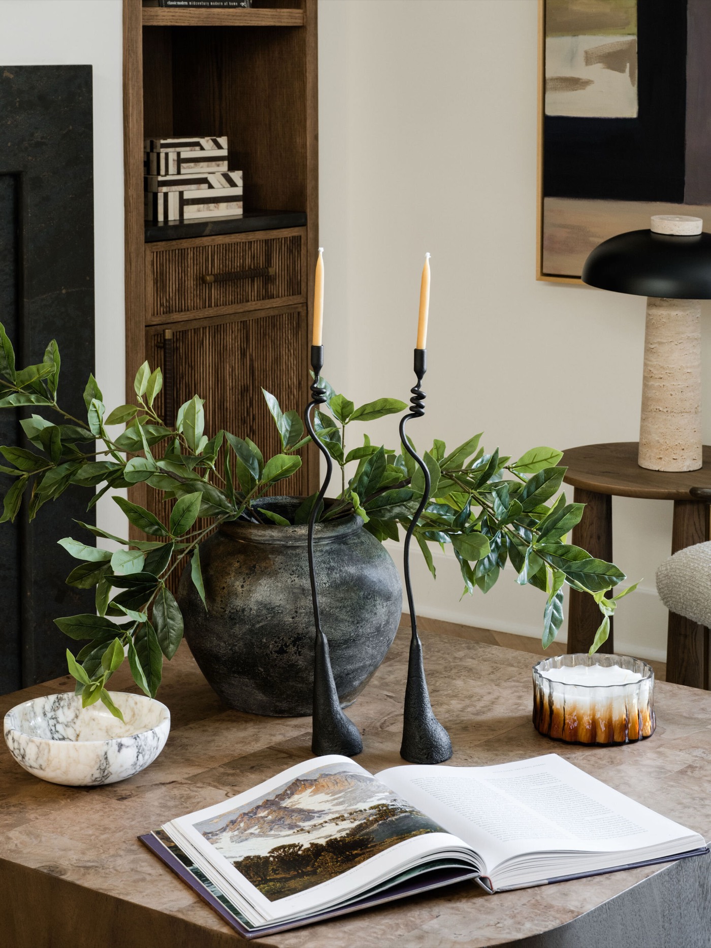 Round wood coffee table styled with black iron candlesticks, a dark ceramic vase of foliage, and a marble bowl, in the Takoma Park project by Jennifer Kizzee Design