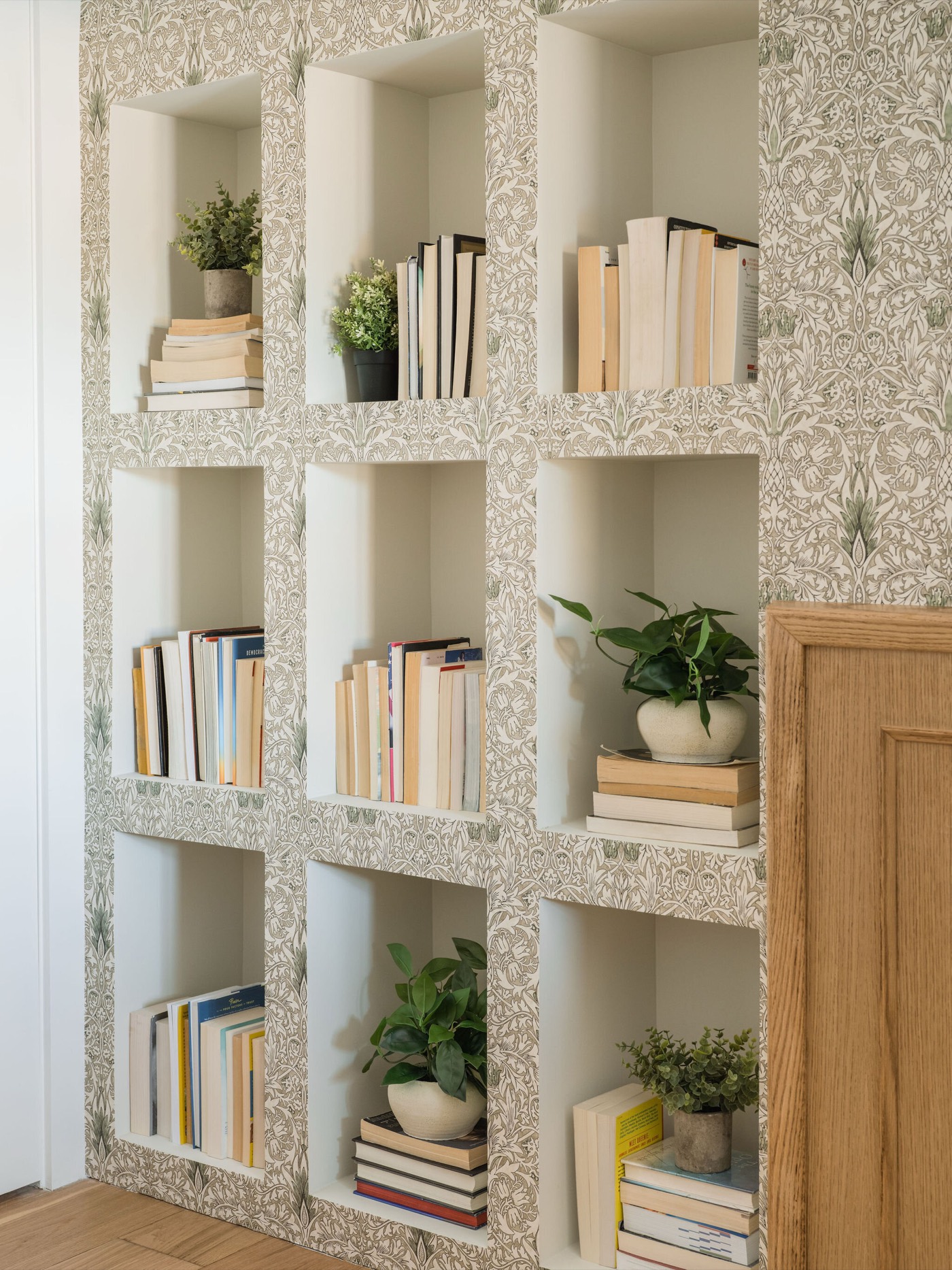 White open cubby bookcase set against a large scale green botanical wallpaper in the Takoma Park project by Jennifer Kizzee Design