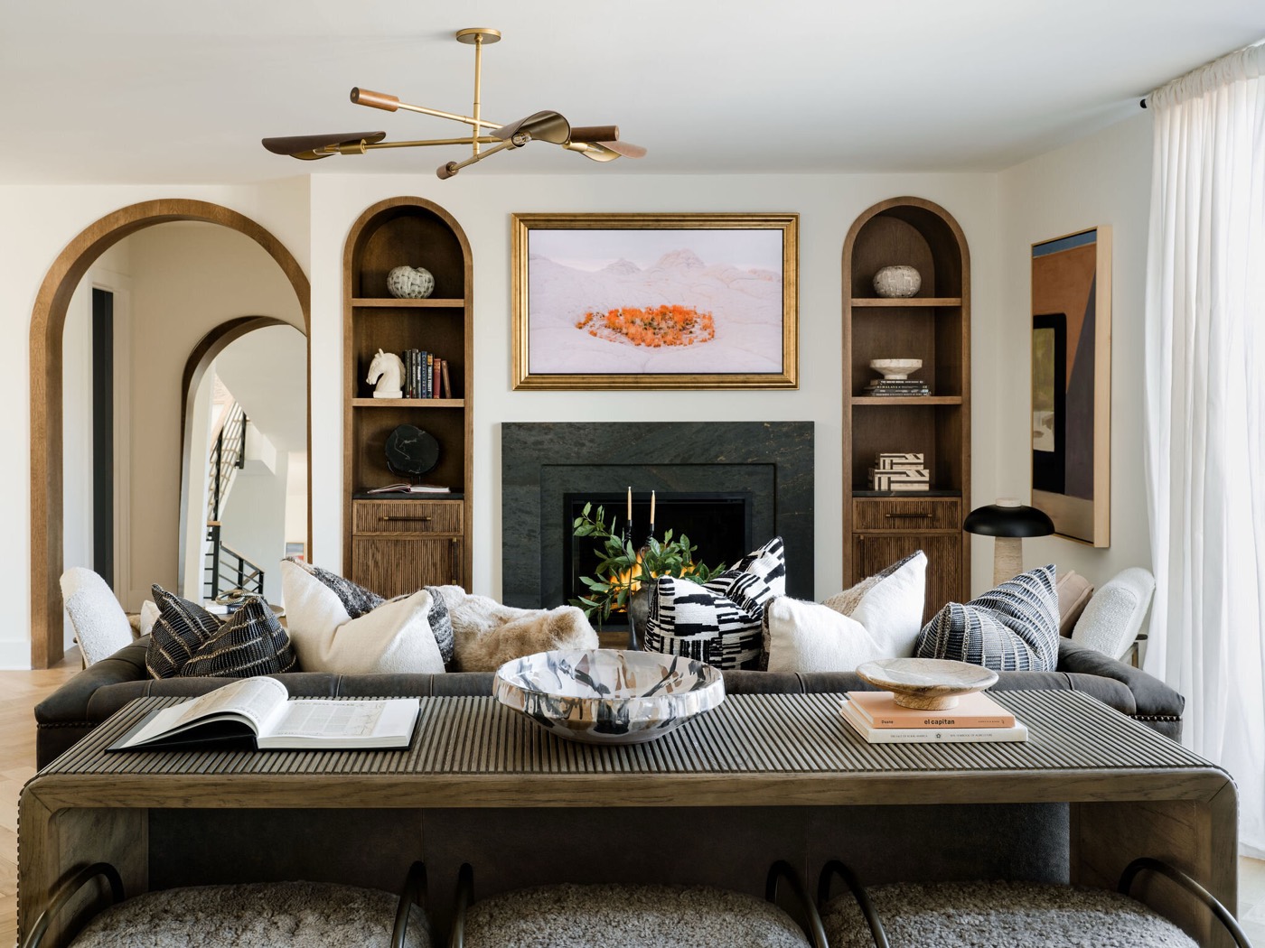 Living room with a dark stone fireplace surround flanked by arched wood niches under a brass arm chandelier in the Takoma Park project by Jennifer Kizzee Design