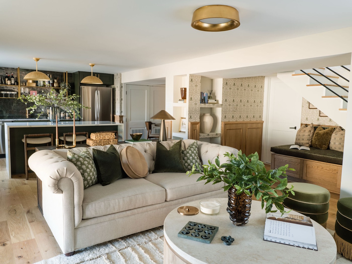 Open lower level linking the green wet bar, a cream roll arm sofa, the wallpapered nook, and the oak stair with its built in bench, in the Takoma Park project by Jennifer Kizzee Design