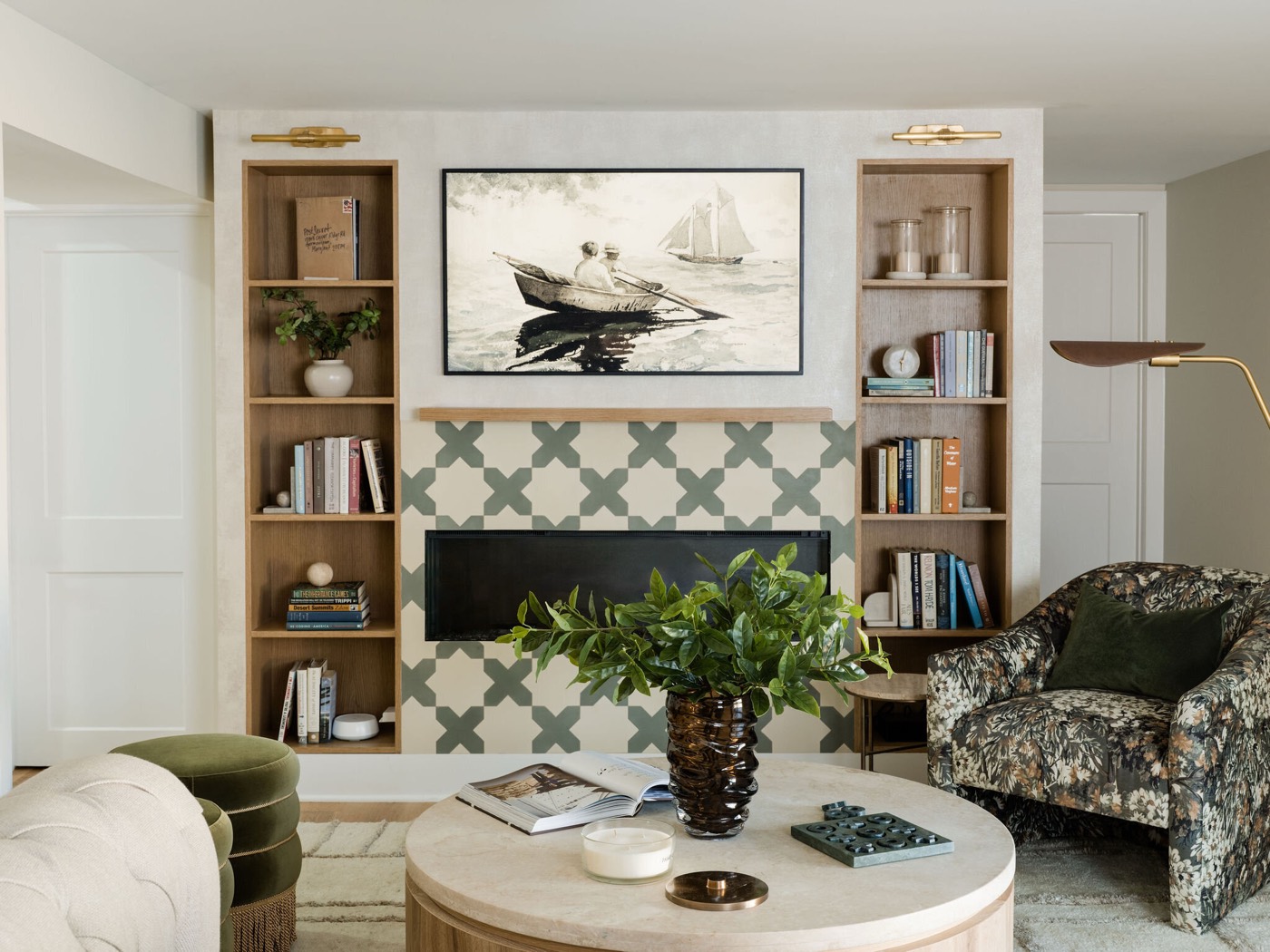 Quatrefoil tile fireplace wall with brass picture lights over oak built ins, facing a floral swivel chair and a stone coffee table, in the Takoma Park project by Jennifer Kizzee Design
