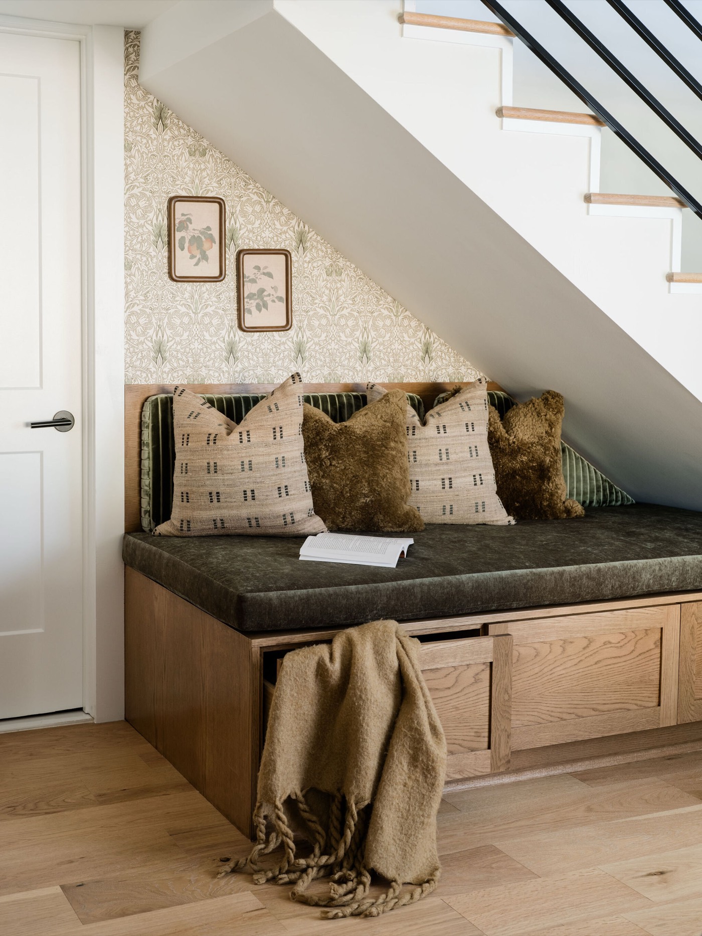 Built in white oak bench with a green velvet cushion tucked under the stair against sprig patterned wallpaper in the Takoma Park project by Jennifer Kizzee Design