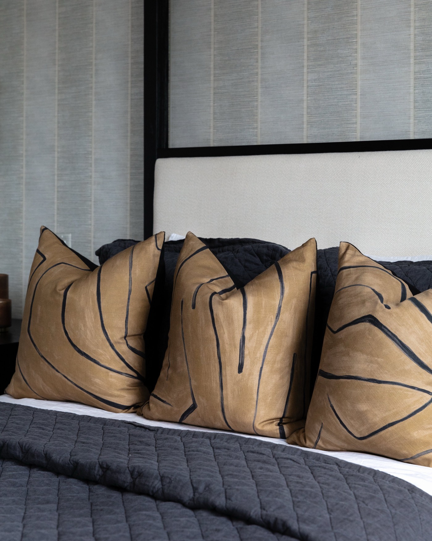 Camel leather pillows with a black line-drawing motif layered against a charcoal quilted coverlet in the Vue Point project by Jennifer Kizzee Design