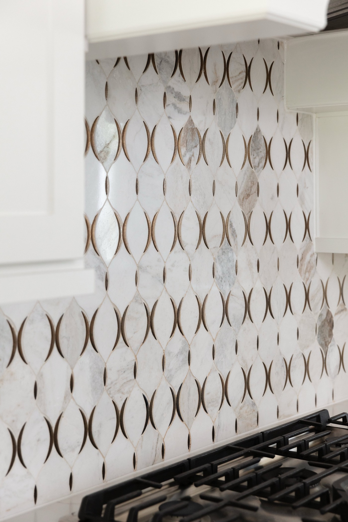 Kitchen backsplash of white marble tile inlaid with brass ovals above a gas cooktop in the Vue Point project by Jennifer Kizzee Design