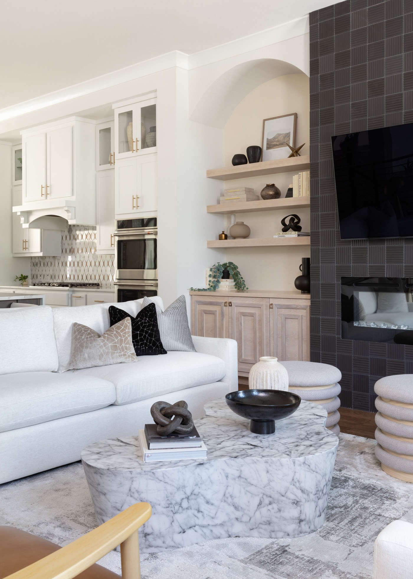Living room with a charcoal tile fireplace, arched niche of white oak shelves, and a sculptural marble coffee table in the Vue Point project by Jennifer Kizzee Design