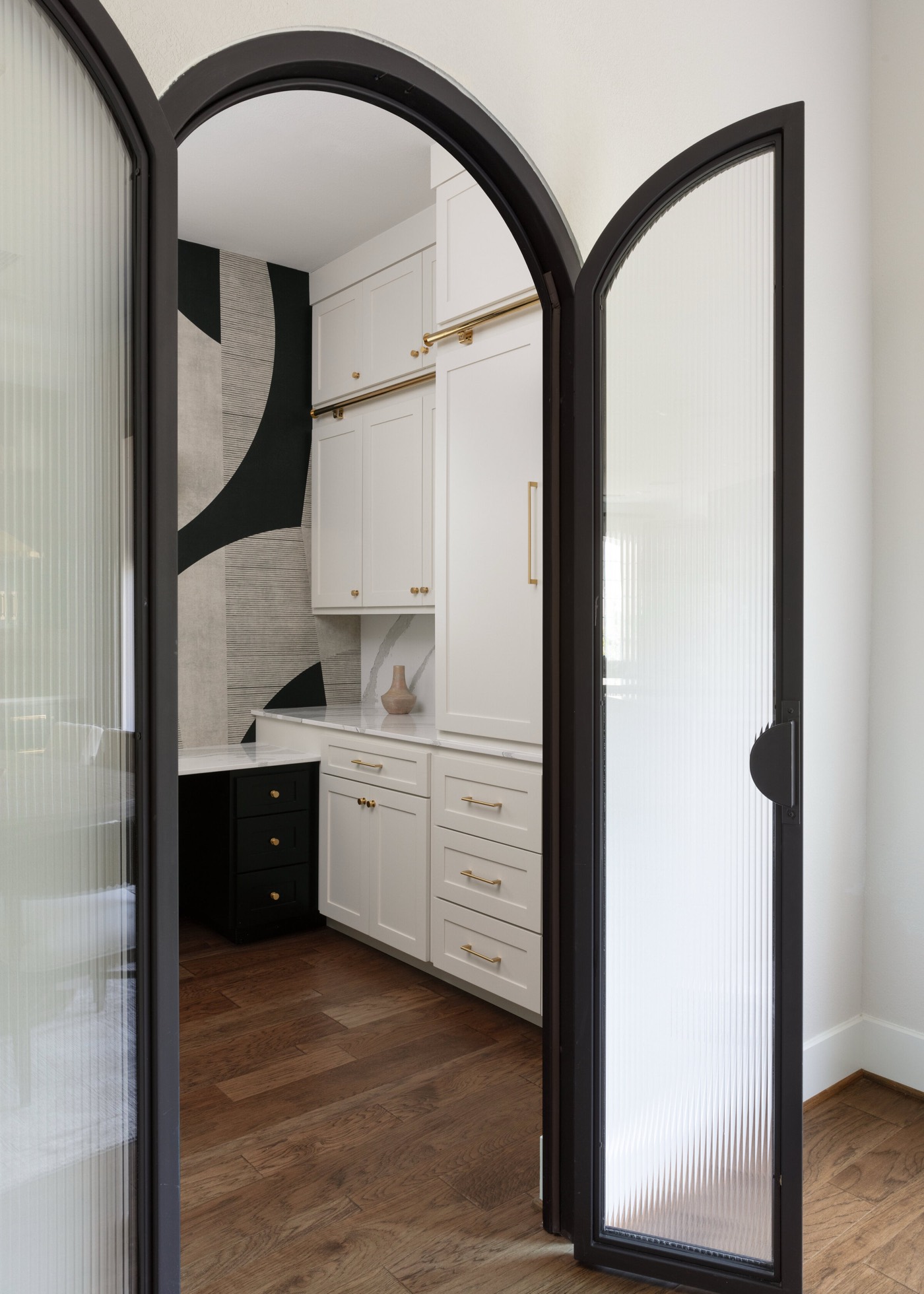 Arched black steel door with reeded glass panels opening into the home office in the Vue Point project by Jennifer Kizzee Design